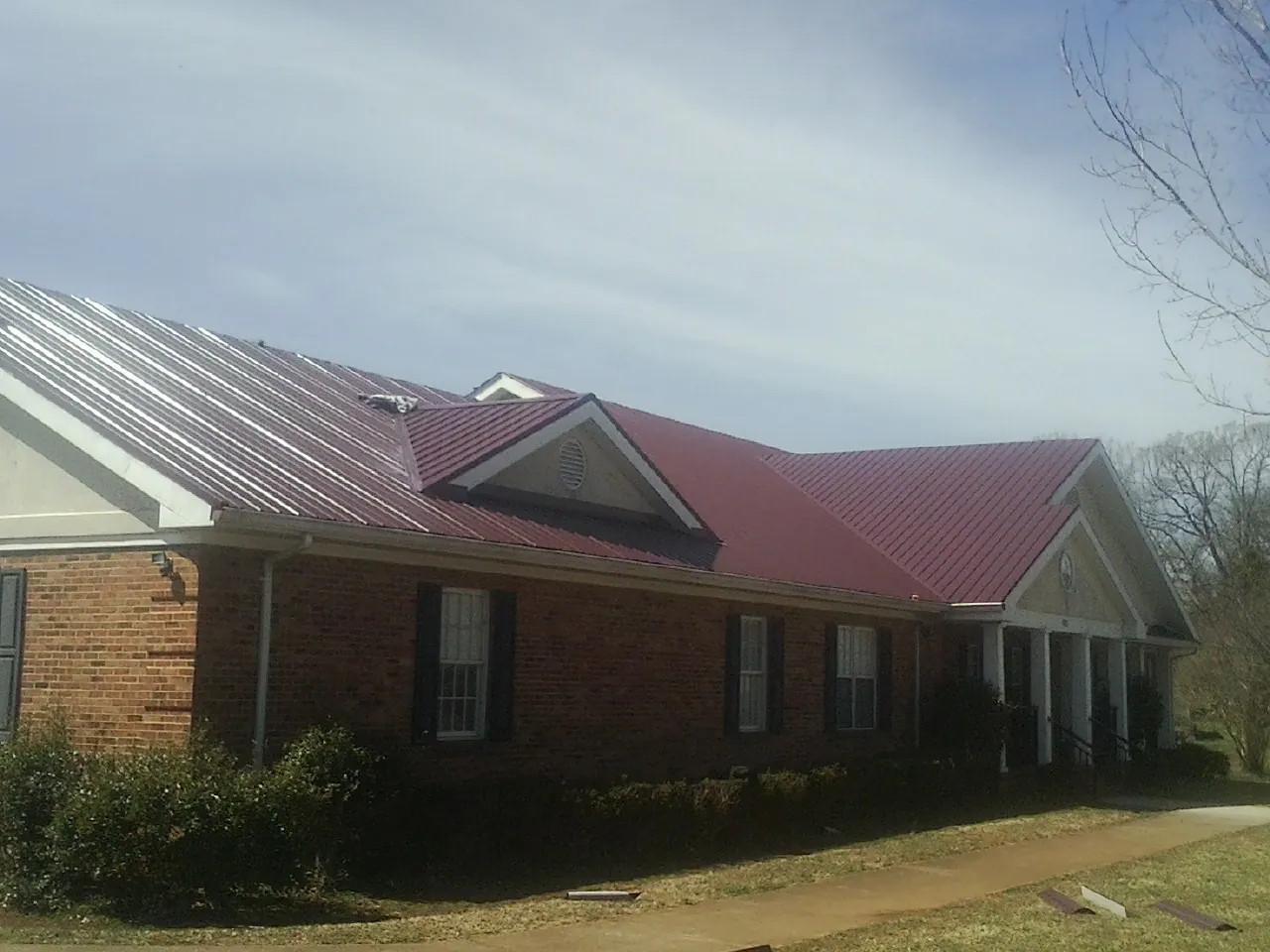 Red metal roof with gabled entries on a long brick building, from a Hail Damage Roof Repair job in Bosque Farms