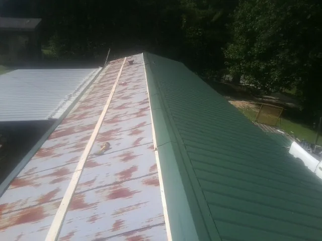Old rusted panels beside newly installed green metal roofing — Wind Damage Roof Repair by Roofing Brothers in Bosque Farms