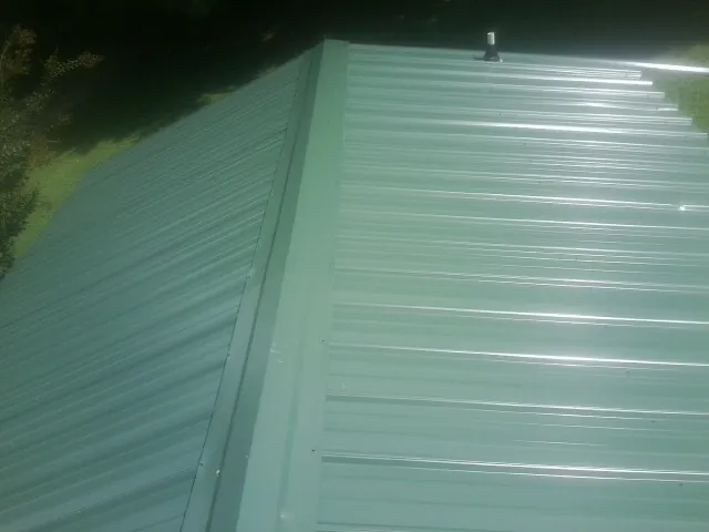 New green metal panels meeting at the ridge of a roof — Flat Roof Repair work by our crew in Bosque Farms