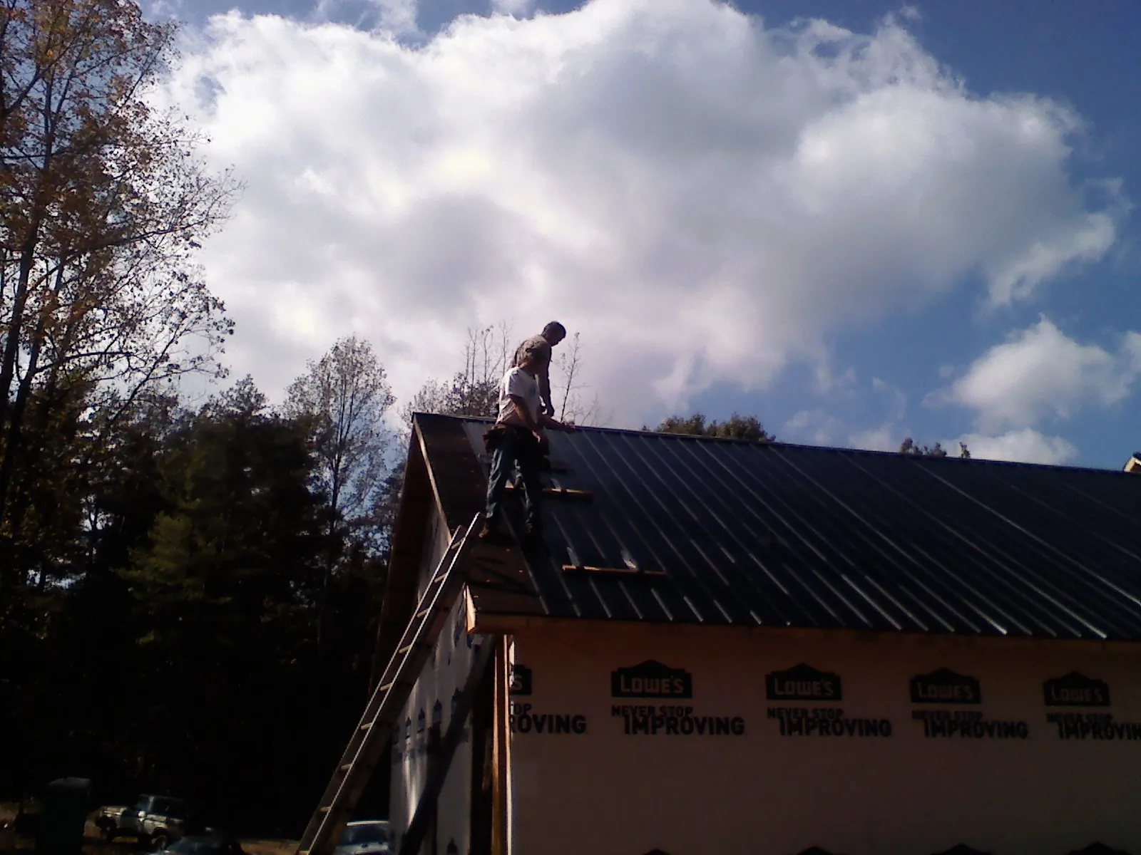 Roofer fastening dark metal panels high against a cloudy sky, from a Roof Inspection job in Bosque Farms