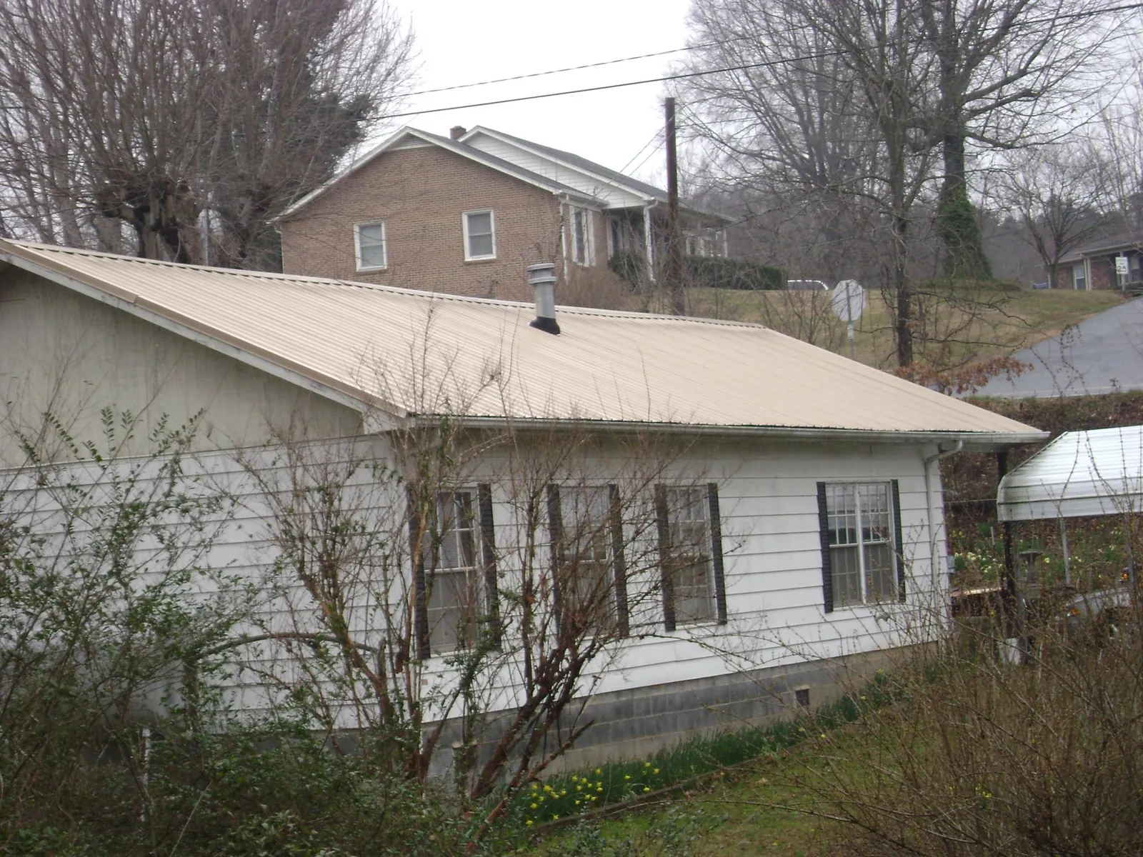 Tan metal roof on a white sided house set into a hillside — Commercial Roofing by Roofing Brothers in Bosque Farms