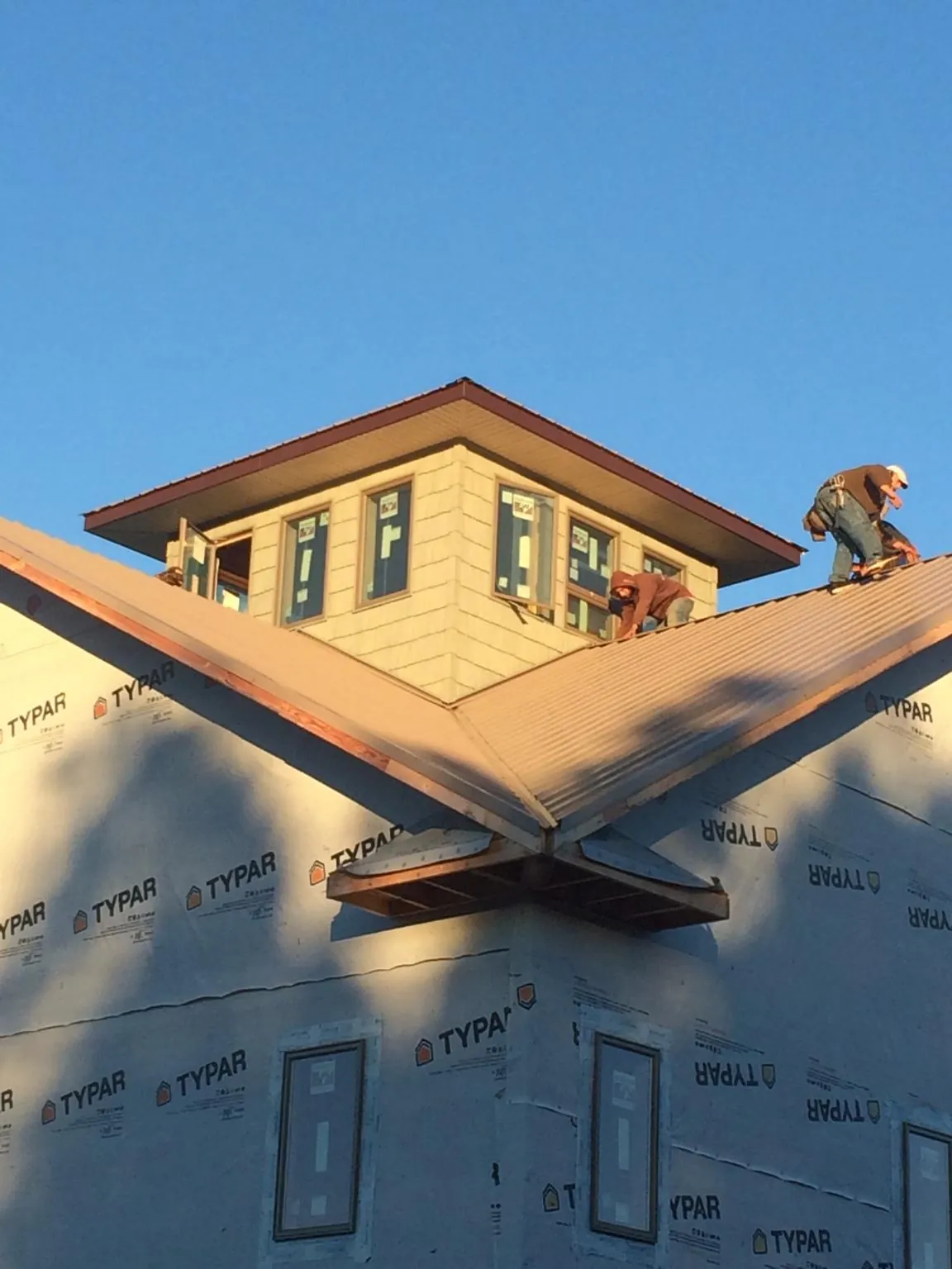 Roofers working around a rooftop cupola on a new metal roof at sunset — Roof Waterproofing in Bosque Farms by Roofing Brothers